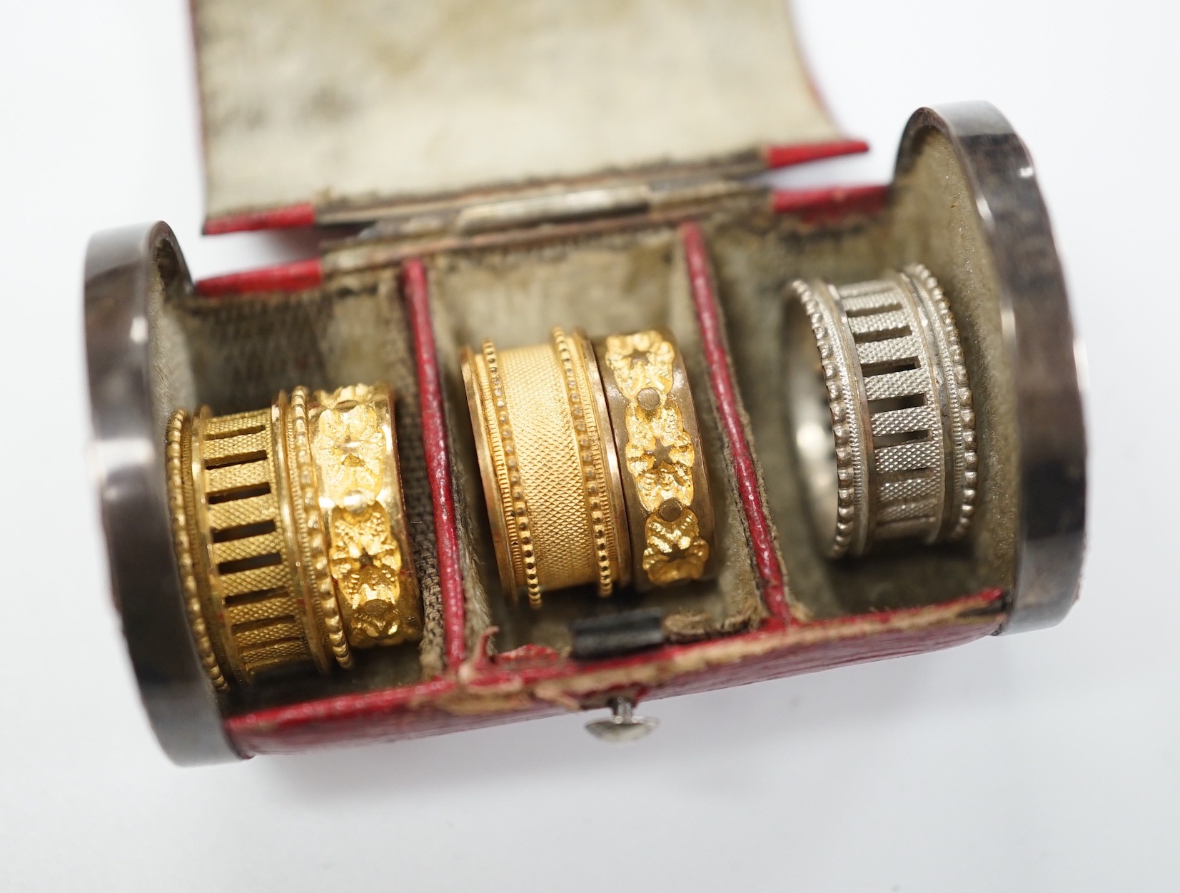 A rare Regency morocco leather mounted white metal cylindrical ring box containing five pinchbeck/base metal sample rings, box length 47mm.